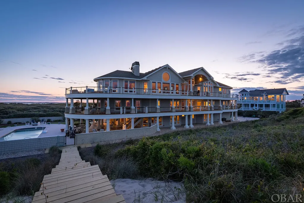 101 Station One Lane Home in Corolla, North Carolina. Discover a remarkable beachfront home with panoramic water views in the prestigious community of Pine Island, Corolla. This stunning coastal retreat offers nine bedrooms with en-suite bathrooms, generous indoor and outdoor amenities, and direct access to 250 feet of secluded beach. 