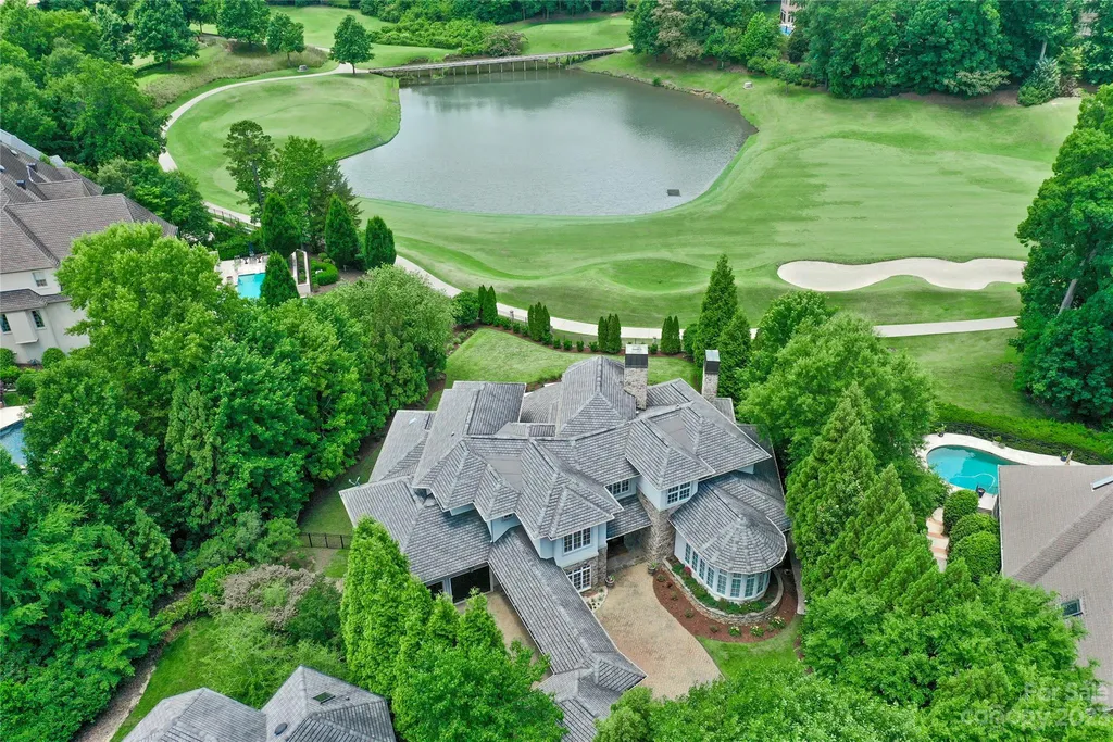 11717 Smart Lane Home in Charlotte, North Carolina. Experience the epitome of modern elegance in this gated estate with breathtaking views of the signature 13th hole from nearly every room and the stunning 48-ft pool. Designed by Christopher Phelps and crafted by Simonini, this home boasts an open floor plan, tall windows, curved walls, and a sweeping custom staircase inspired by Art Deco design.