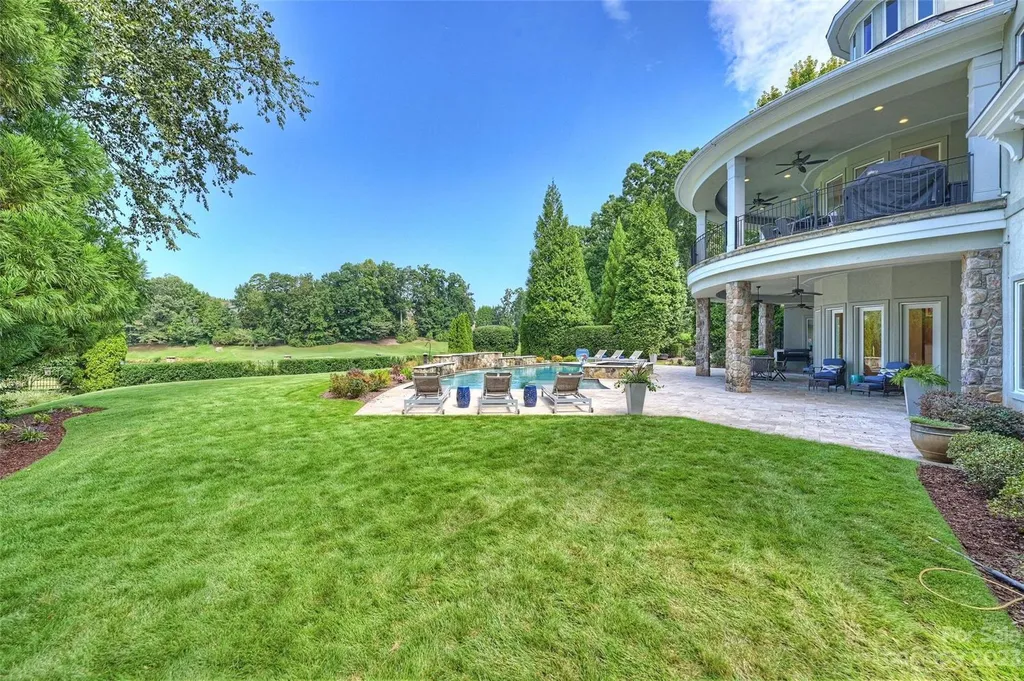 11717 Smart Lane Home in Charlotte, North Carolina. Experience the epitome of modern elegance in this gated estate with breathtaking views of the signature 13th hole from nearly every room and the stunning 48-ft pool. Designed by Christopher Phelps and crafted by Simonini, this home boasts an open floor plan, tall windows, curved walls, and a sweeping custom staircase inspired by Art Deco design.