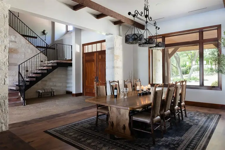 The formal dining area with a long wooden table, a unique wrought-iron chandelier, and an adjacent stone and iron staircase leading to the upper floor.