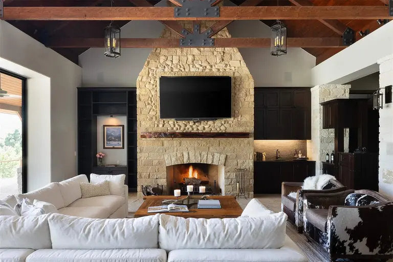 A warm family room with a towering, full-height stone fireplace, rustic wooden beams on the high ceiling, and comfortable seating, ideal for cozy evenings.