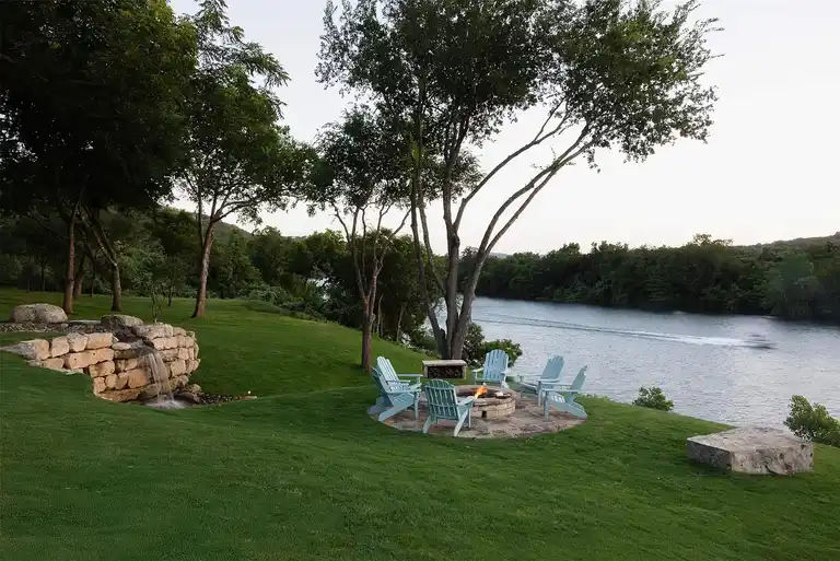 The expansive pool area and covered patio of a **luxury home in Austin**, featuring a rectangular pool with mosaic tiles, an outdoor bar, dining area, and lush green hillside backdrop, highlighting an **expensive home in Austin**.