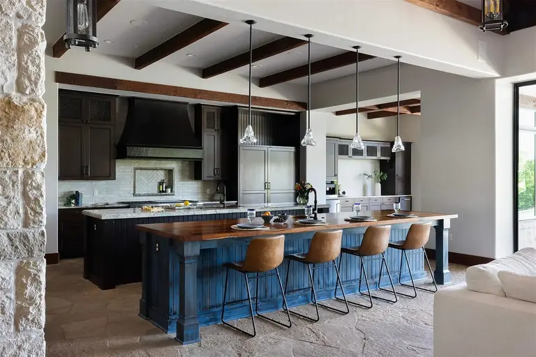 The gourmet kitchen featuring a large white stone island, dark custom cabinetry, professional stainless steel appliances, and sleek marble backsplashes, a key feature in an **expensive home in Austin**.