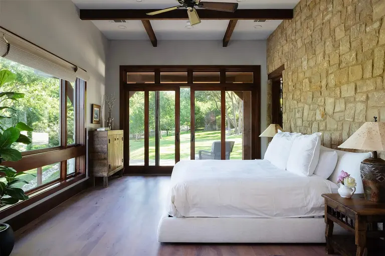 The expansive master suite featuring a slatted wooden vaulted ceiling, minimalist design, and an adjacent sitting area with floor-to-ceiling windows.
