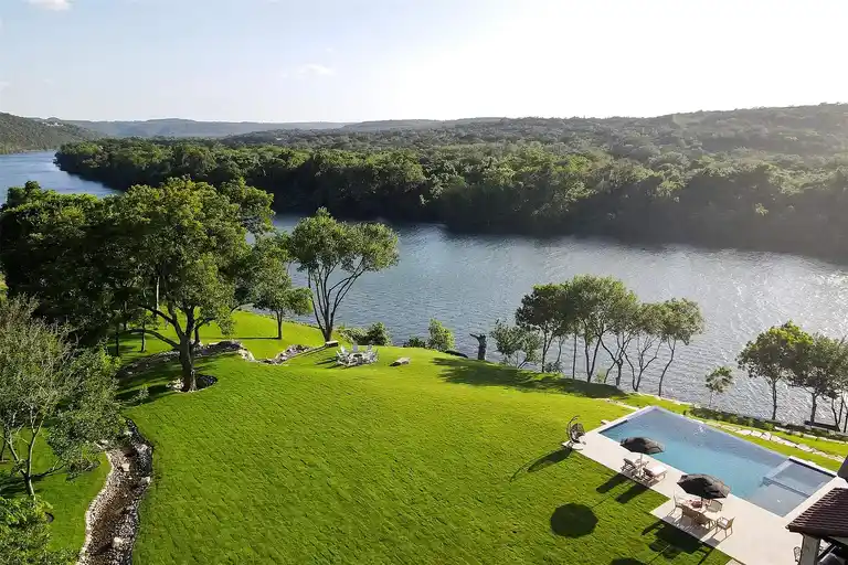 An aerial view of the expansive lawn and resort-style pool of the **luxury home in Austin**, with direct views of Lake Austin and surrounding greenbelt.