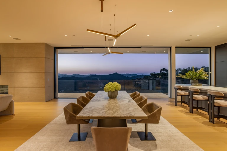 Formal dining area with a long marble table and custom lighting, situated directly in front of a floor-to-ceiling window overlooking the canyon.