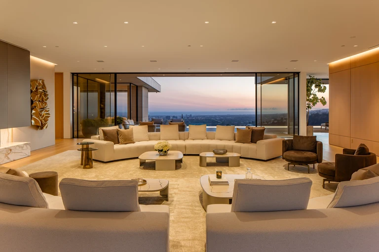 Main living room at sunset featuring minimalist furniture, fireplace, and massive sliding glass doors opening to the panoramic view deck.