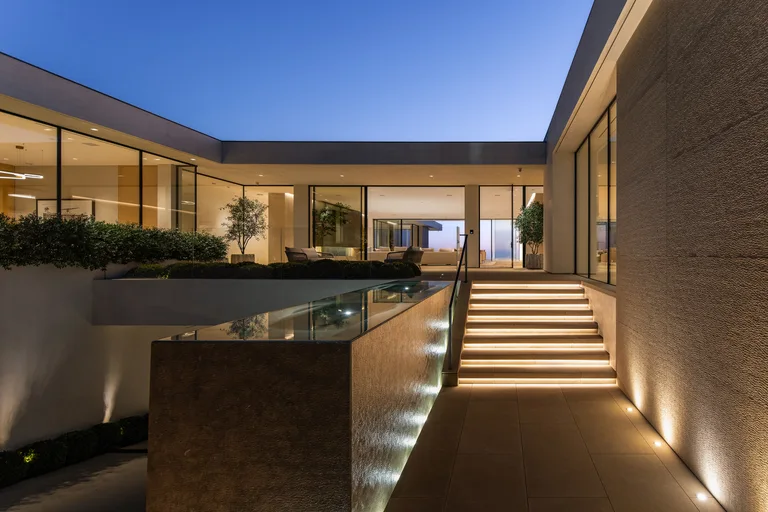 Open-plan great room with a skylight, marble kitchen island, dining area, and full-width glass walls showcasing the view.