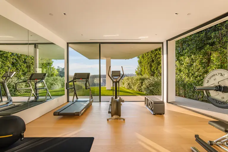 Day-lit home fitness center featuring Technogym equipment, a mirrored wall, and floor-to-ceiling glass opening to the green space.