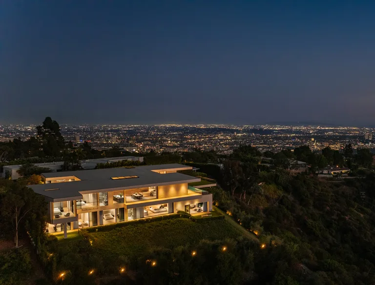 Night aerial view of The View Estate showcasing the illuminated facade and floor-to-ceiling glass walls with jetliner views of Los Angeles.