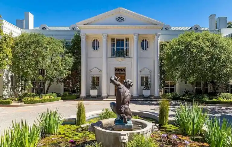 Casa Encantada main facade featuring Neoclassical architecture, white columns, and a bronze cherub statue fountain in the driveway