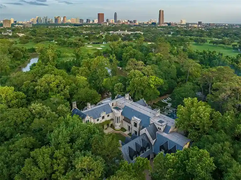 Aerial view of The Lodge at Hunters Creek, the most expensive home in Houston, Texas, surrounded by lush greenery with the Houston skyline in the background.