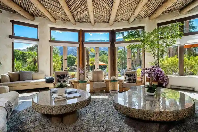 The main living room of the Steve Chase design, featuring a monumental central fireplace, custom curved seating, a circular stone coffee table, and the signature exposed log ceiling.