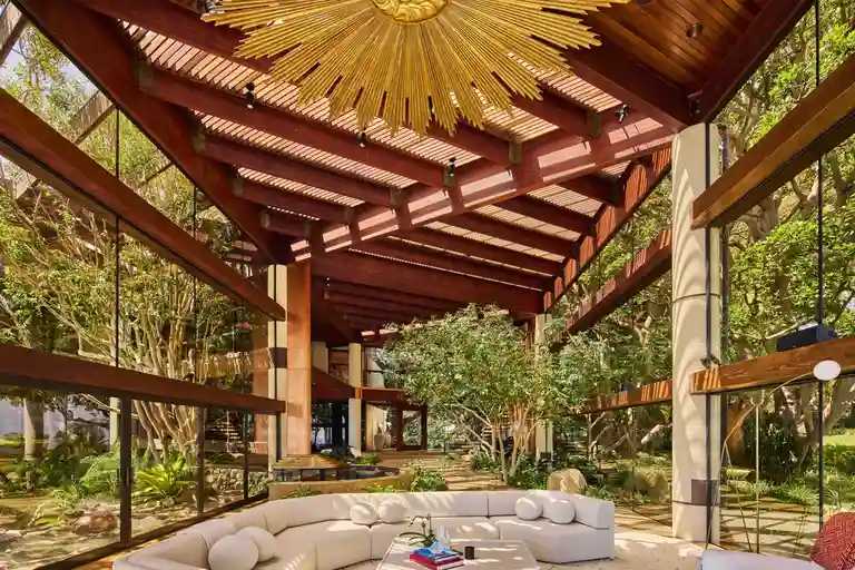 Interior living room in the Arboretum Pavilion with soaring wood-slat ceiling, floor-to-ceiling glass walls, and interior trees, at 6962 Wildlife Rd.