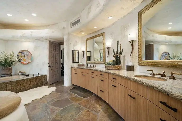 Primary bathroom with curved wooden vanity, granite countertops, dual mirrors, flagstone flooring, and a unique stone bathtub, reflecting the design of 475 S Via Las Palmas, a luxury home Palm Springs.