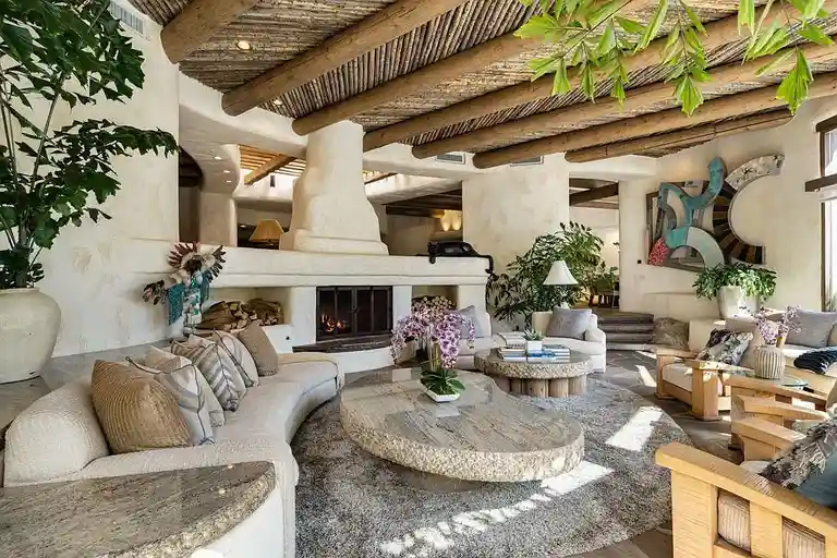 Another view of the expansive living room designed by Steve Chase, showcasing its dramatic fireplace, unique coffee table, and abundant natural light filtering through, characteristic of this most expensive home in Palm Springs.