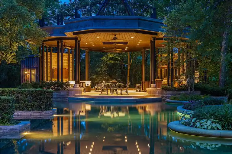 Illuminated luxury outdoor gazebo pavilion surrounded by a reflecting water feature at The Lodge, the **most expensive home in Houston**, offering a private nighttime entertainment oasis.