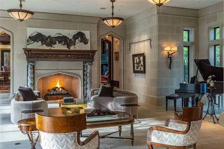 Interior view of the elegant living room in The Lodge, the **most expensive home in Houston**, featuring a grand carved fireplace, limestone walls, and bespoke luxury furnishings.