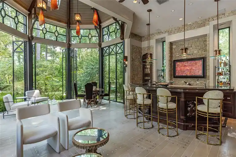 Luxury entertainment area and wet bar in The Lodge, the **most expensive home in Houston**, featuring stone walls, full-height glass windows, and seamless integration with the surrounding greenery