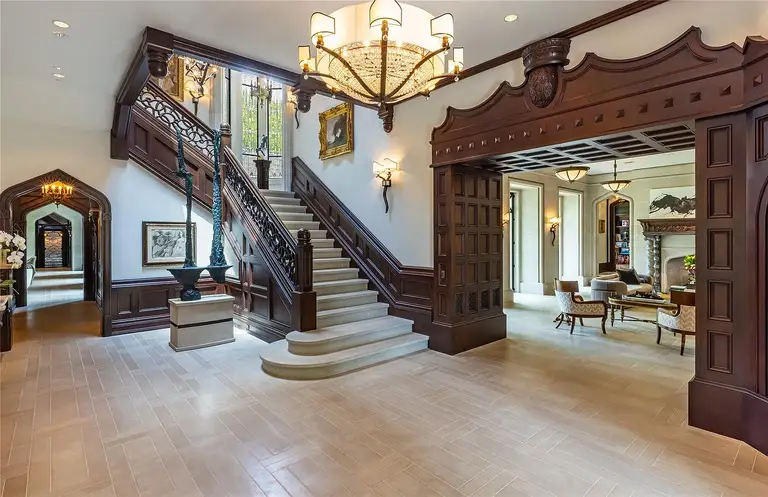 Grand entry foyer and two-story staircase of The Lodge, the most expensive home in Houston, featuring dark wood paneling, stone floors, and a magnificent chandelier.