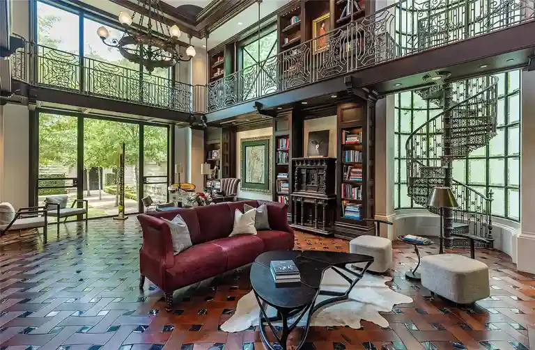 Two-story library and study in The Lodge, the **most expensive home in Houston**, featuring a wrought iron spiral staircase, built-in bookshelves, and an upper viewing balcony.