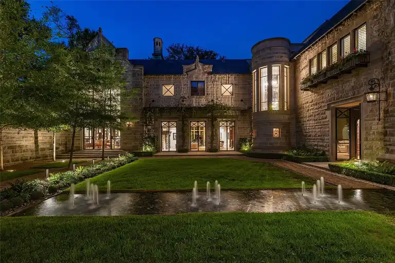 Night view of The Lodge at Hunters Creek, the most expensive home in Houston, with illuminated facade, manicured lawns, and elegant water fountains.