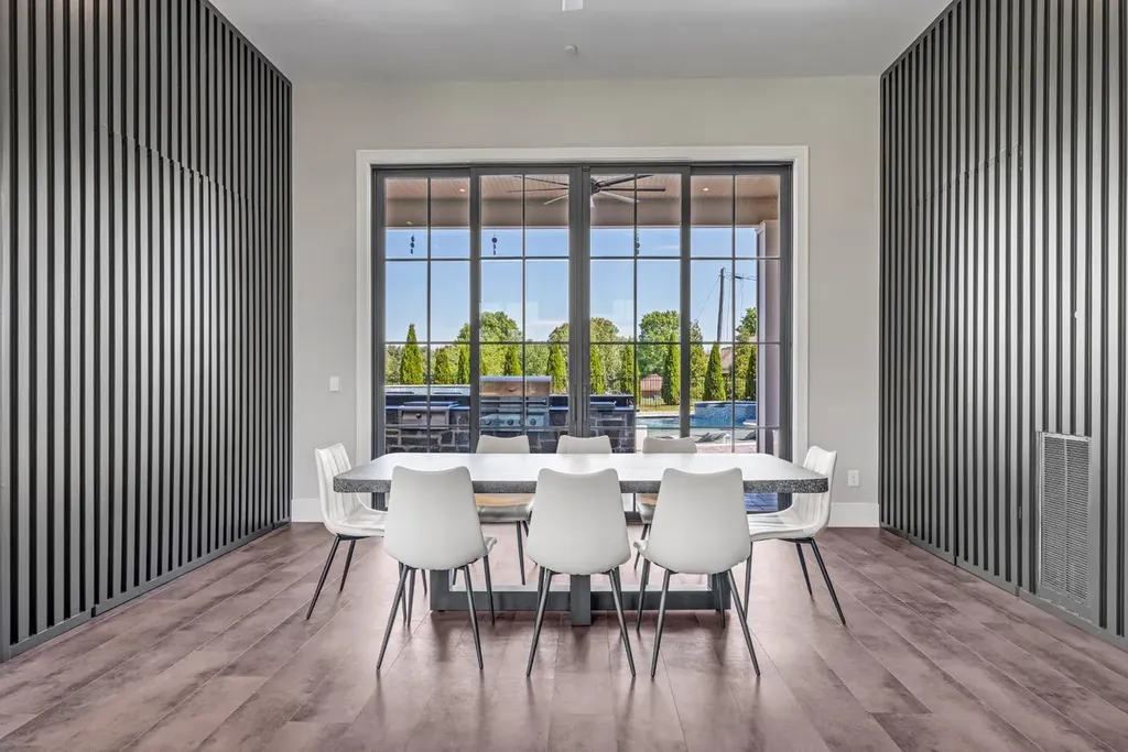 Minimalist dining room with modern white chairs, marble table, and floor-to-ceiling windows overlooking the pool at a Mount Juliet luxury home.