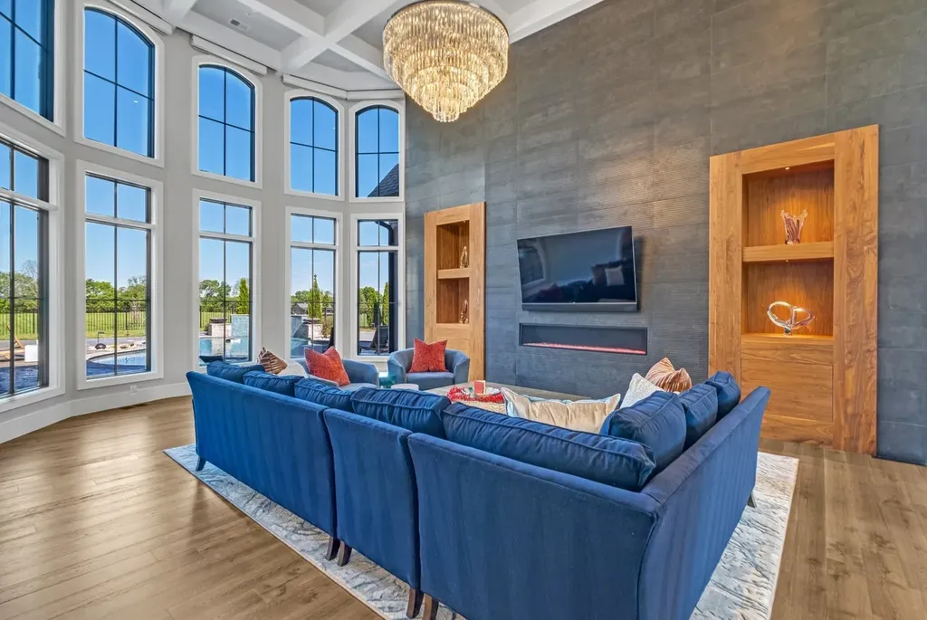 Great room with floor-to-ceiling windows, blue sectional sofa, chandelier, and modern fireplace at a luxury home in Mount Juliet, Tennessee.