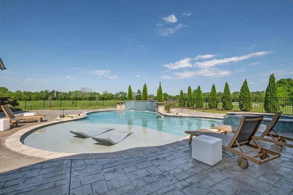 Luxury pool area with sun loungers, shallow tanning ledge, and water feature overlooking open landscape in Mount Juliet, Tennessee.