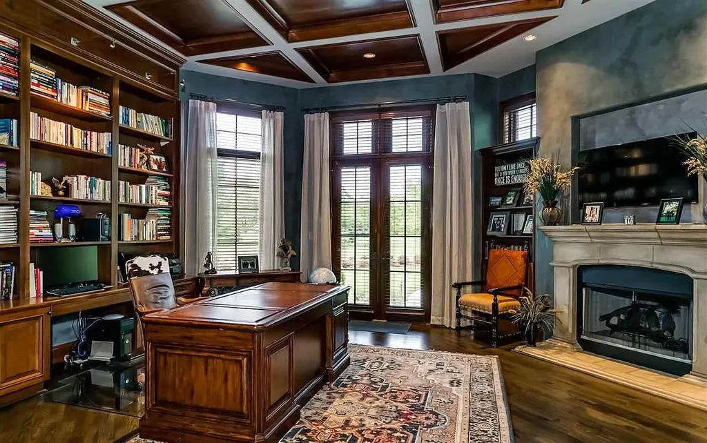 Luxury home office at 2470 Cahaba Valley Rd, Indian Springs, Alabama, featuring custom wood cabinetry, coffered ceiling, fireplace, and French doors overlooking the estate grounds, as seen in Luxury Houses Magazine.