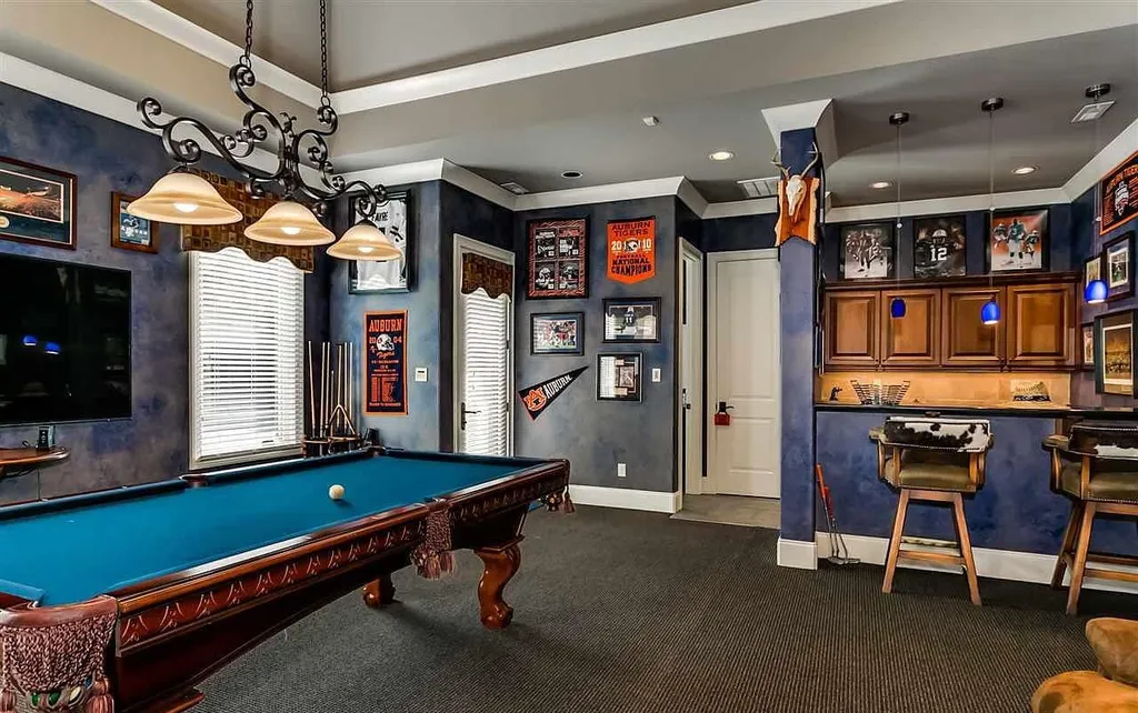 Luxury game room at 2470 Cahaba Valley Rd, Indian Springs, Alabama, featuring a custom billiard table, sports memorabilia, home bar, and ambient lighting, featured in Luxury Houses Magazine.