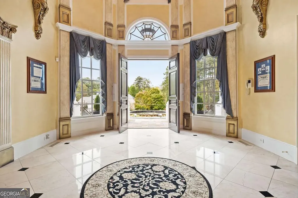The main foyer entrance looking outward through the large open double doors towards the front fountain and circular drive, featuring a black and white marble floor.