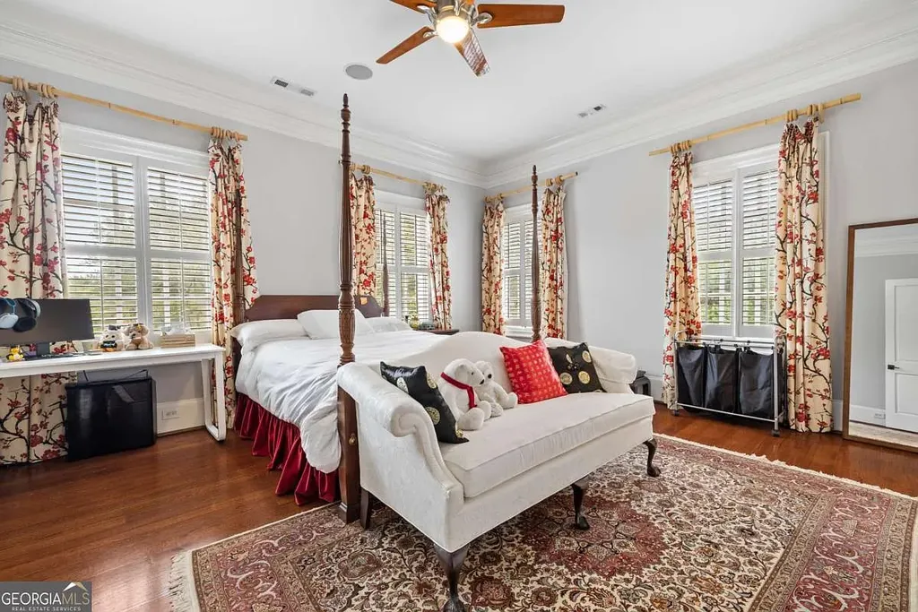 A bright, secondary bedroom in the Atlanta White House, featuring hardwood floors, a four-poster bed, a decorative rug, and large windows with patterned curtains