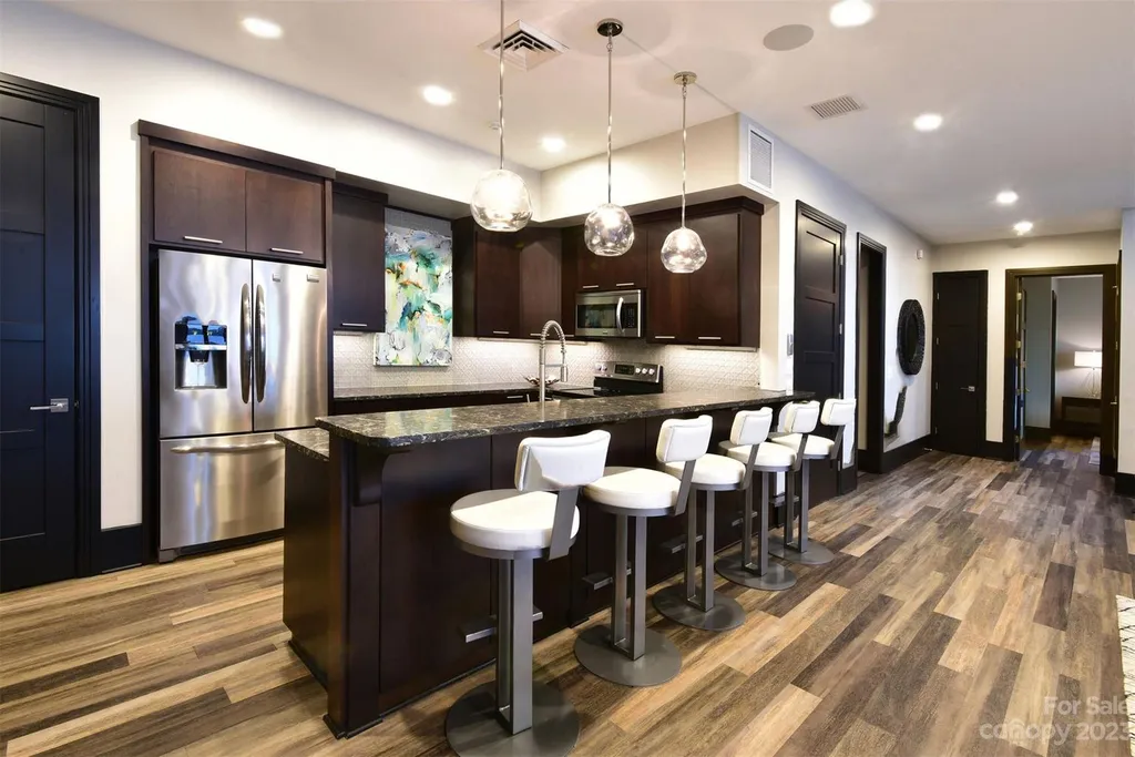 A Breathtaking Modern Masterpiece Overlooking Lake Tillery, North Carolina 10 Secondary kitchen at 4059 Old Timber Way, Norwood, North Carolina, featuring sleek dark cabinetry, granite countertops, pendant lighting, and bar seating design.