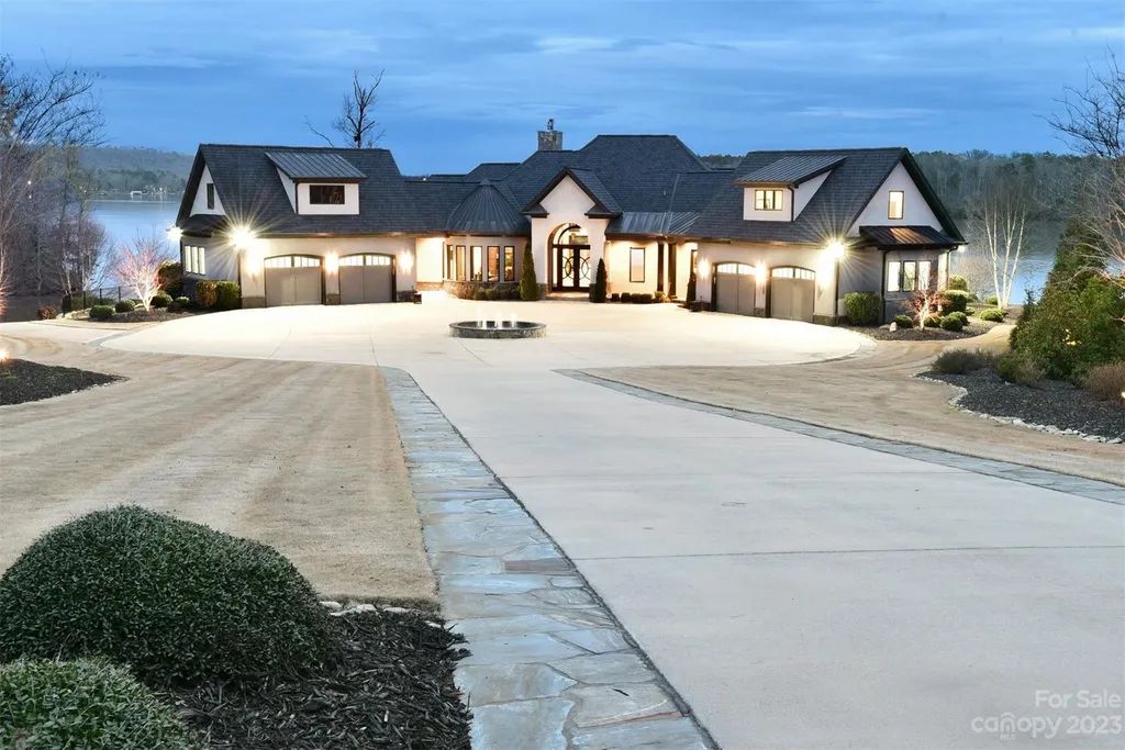 A Breathtaking Modern Masterpiece Overlooking Lake Tillery, North Carolina 13 Front exterior view of 4059 Old Timber Way, Norwood, North Carolina, with circular driveway, manicured landscaping, and lakefront backdrop at dusk.