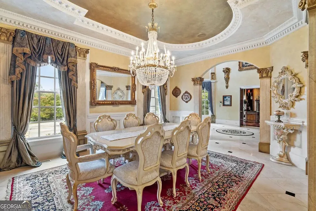 The luxurious formal dining room inside the Atlanta White House, featuring gold accents, elaborate ceiling trim, a crystal chandelier, and large windows.