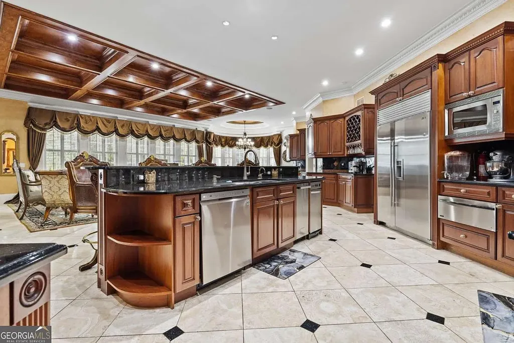 The gourmet chef's kitchen inside the Atlanta White House, featuring dark wood cabinetry, stainless steel appliances, a large black granite island, and coffered ceilings.