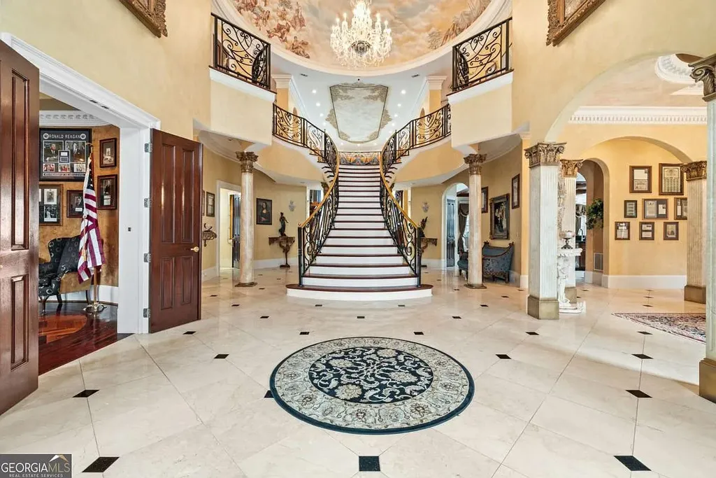 The main grand foyer of the Atlanta White House, featuring a sweeping statement staircase, marble floors, Corinthian columns, and an elaborate ceiling mural.