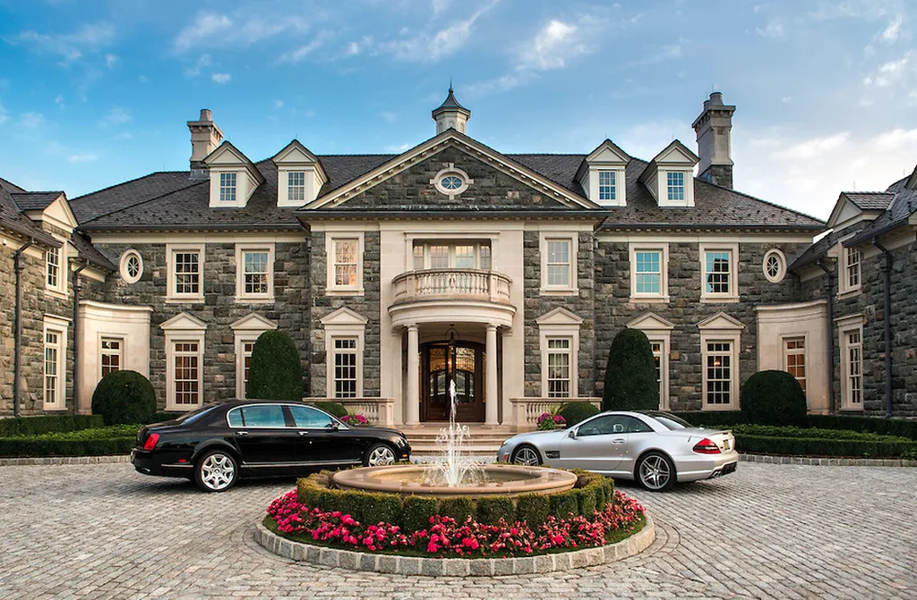Step Inside One of America’s Most Extraordinary Modern Estates in Alpine 3 Luxury entrance of 1 Frick Drive in Alpine New Jersey featuring a circular fountain exotic cars and a stately stone mansion façade.