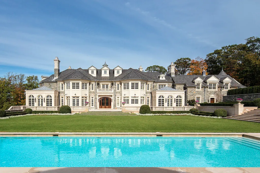Step Inside One of America’s Most Extraordinary Modern Estates in Alpine 12 Rear view of the grand luxury mansion at 1 Frick Drive Alpine New Jersey featuring symmetrical architecture manicured lawns and a large sparkling pool in the foreground.