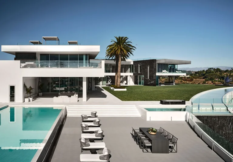 Luxury outdoor living space at The One, the biggest home in Los Angeles, featuring patio furniture, an exterior pool deck, and modern white architecture.