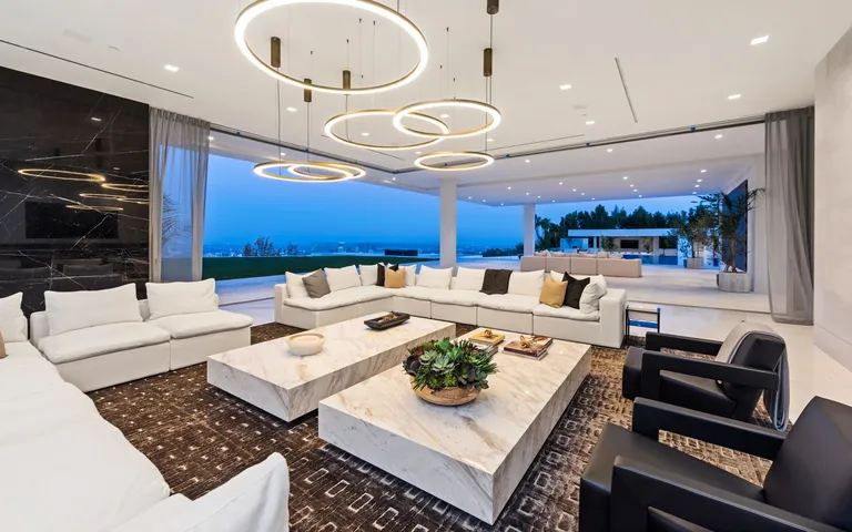 The spacious, open-plan great room inside The One, featuring modern white and black seating, marble tables, and seamless access to the exterior terrace.