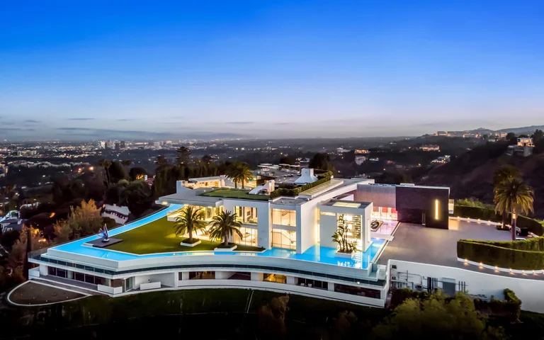 The One, the biggest home in Los Angeles, at dusk, showcasing the iconic wraparound infinity pool and modern white exterior architecture