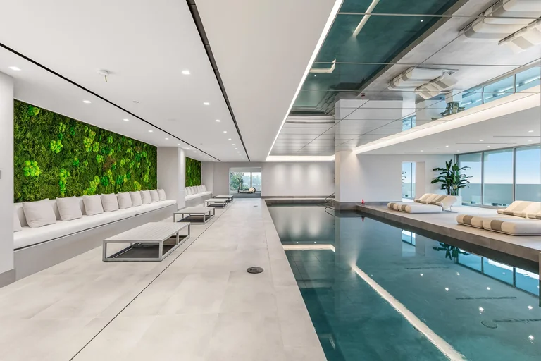 The serene indoor spa pool and lounging area inside The One, the biggest home in Los Angeles, featuring a green moss wall and white, minimalist design.