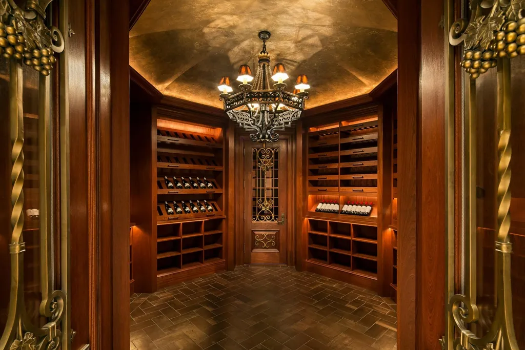 Step Inside One of America’s Most Extraordinary Modern Estates in Alpine 6 Luxurious wine cellar at 1 Frick Drive in Alpine New Jersey featuring custom wood shelving warm lighting and an ornate iron door.