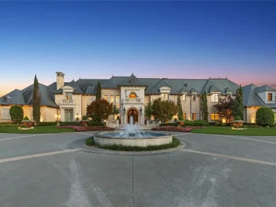 Château Lumièr in McKinney Lists for $14.65 Million as a French Chateau Estate Spanning Fifteen Wooded Acres 1 Front exterior of Château Lumièr at 1201 Gray Branch Rd in McKinney featuring French Chateau architecture a circular motor court and a central fountain at twilight.