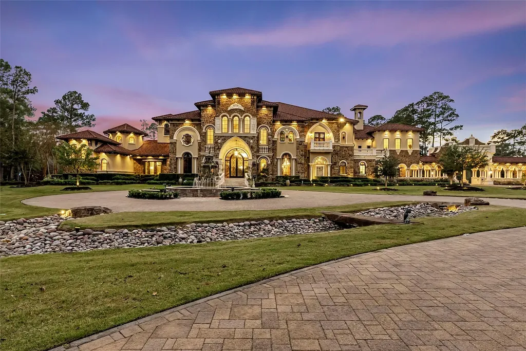 A Mediterranean Masterpiece Rising Above the Woodlands of Magnolia, Texas Seeks for $11,500,000 3 Twilight front elevation of the Mediterranean mansion at 38262 Windy Ridge Trail in Magnolia, Texas, featuring warm exterior lighting, arched windows, stone façade, manicured landscaping, and a grand circular drive.