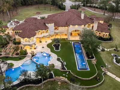 A Mediterranean Masterpiece Rising Above the Woodlands of Magnolia, Texas Seeks for $11,500,000 1 Aerial twilight view of the Mediterranean estate at 38262 Windy Ridge Trl in Magnolia, Texas, featuring tiered resort-style swimming pools, illuminated lap pool, expansive terraces, balconies, and manicured grounds.