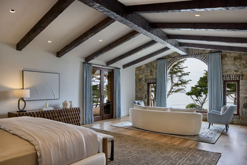 Oceanfront Masterwork Listed at 43 Million Presents One of Southern California’s Most Extraordinary Blufftop Estates 7 Primary bedroom of the oceanfront estate at 4130 Calle Isabella featuring exposed beams, stone arch window, coastal views, and contemporary Mediterranean design.