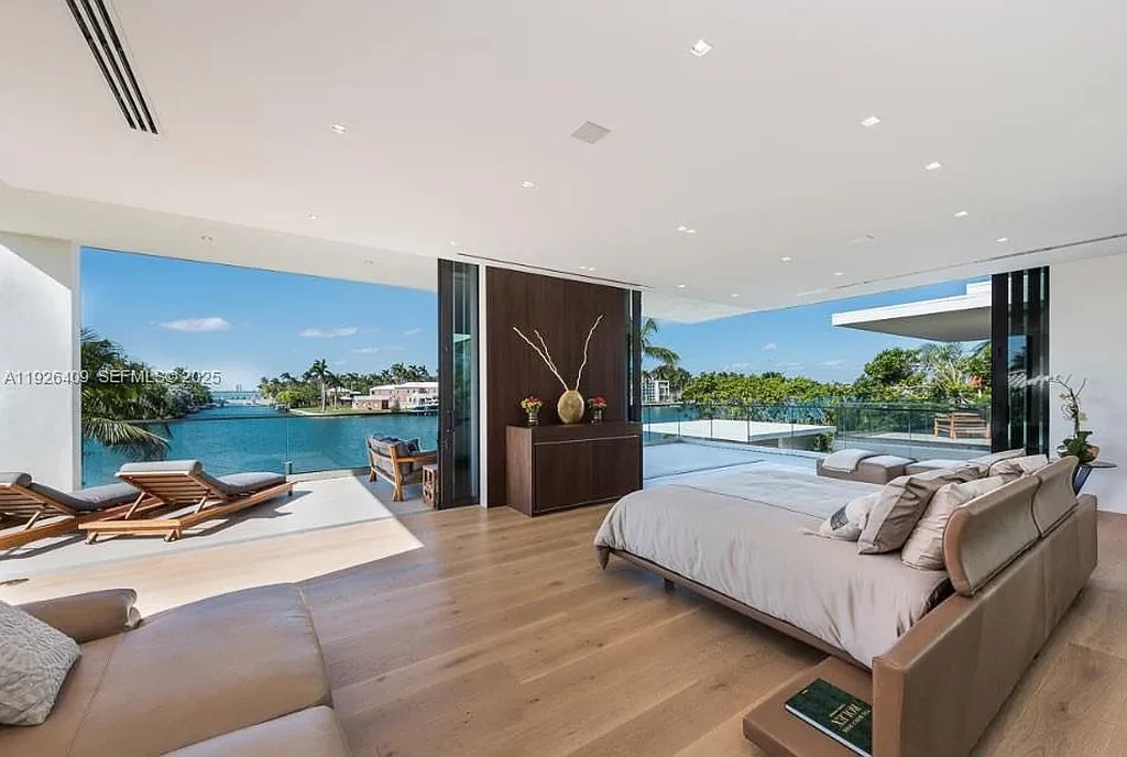 Waterfront exterior view of a tropical modern luxury residence at 6480 Allison Rd in Miami Beach, featuring floor-to-ceiling glass, resort-style pool, and bayfront access.